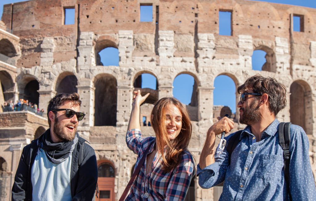 Three happy young friends tourists in front of colosseum in rome